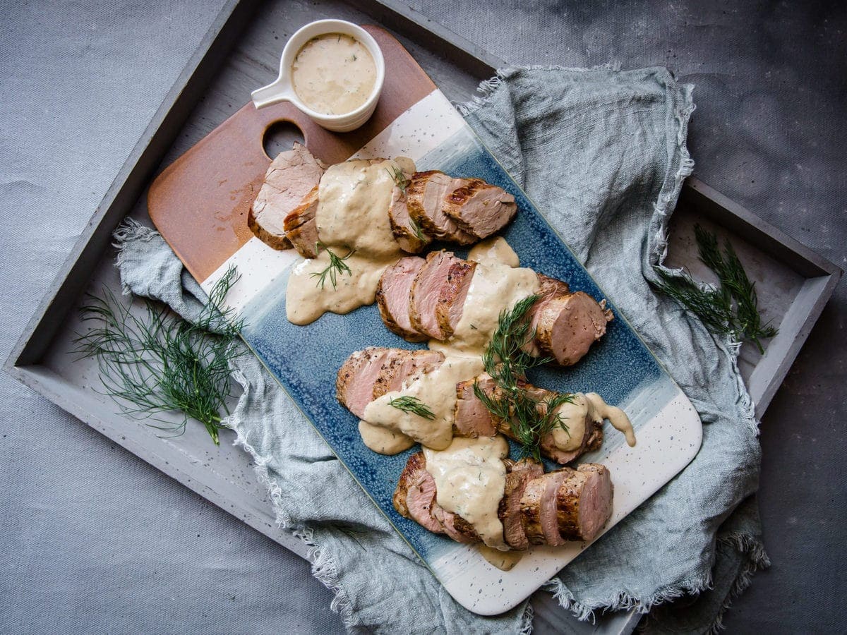 a blue serving tray with pork tenderloin medallions, topped with a creamy sauce and fresh dill