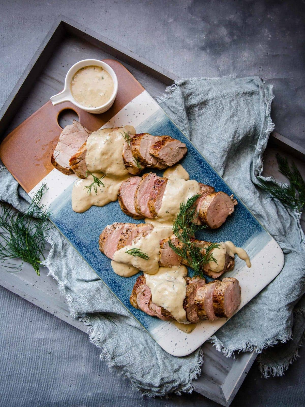 a blue serving tray with pork tenderloin medallions, topped with a creamy sauce and fresh dill