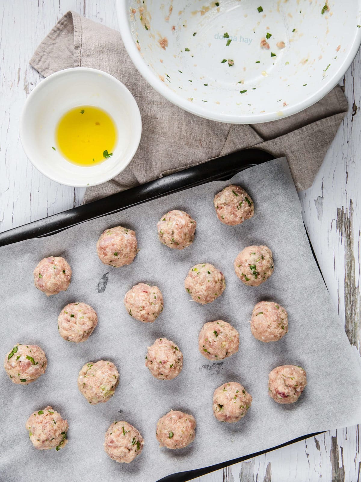 a sheet pan lined with parchment paper and topped with raw chicken meatballs, ready to be baked. 