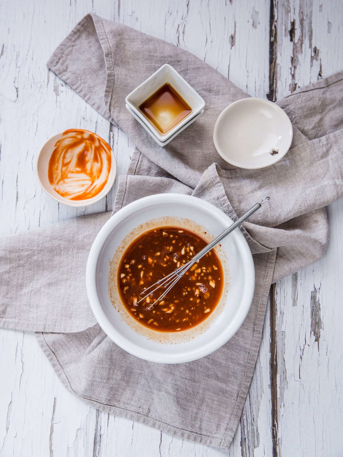 a white bowl with ingredients for an asian dipping sauce - sweetener, garlic, hot sauce, soy sauce