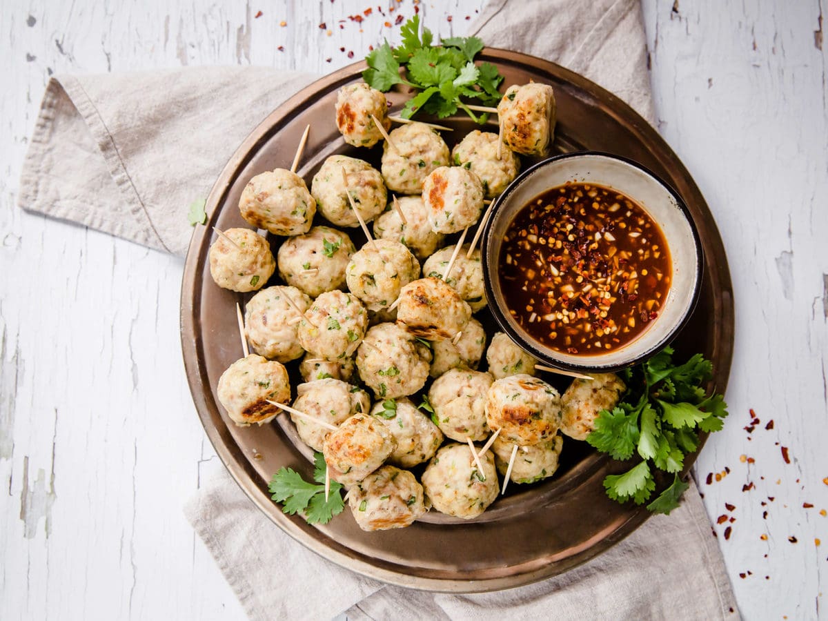 a plate of Asian chicken meatballs with toothpicks, served with dipping sauce and garnished with cilantro