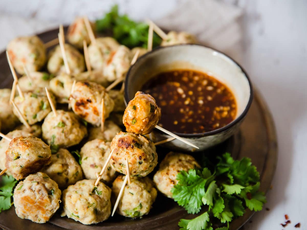 a plate of Asian chicken meatballs with toothpicks, served with dipping sauce and garnished with cilantro
