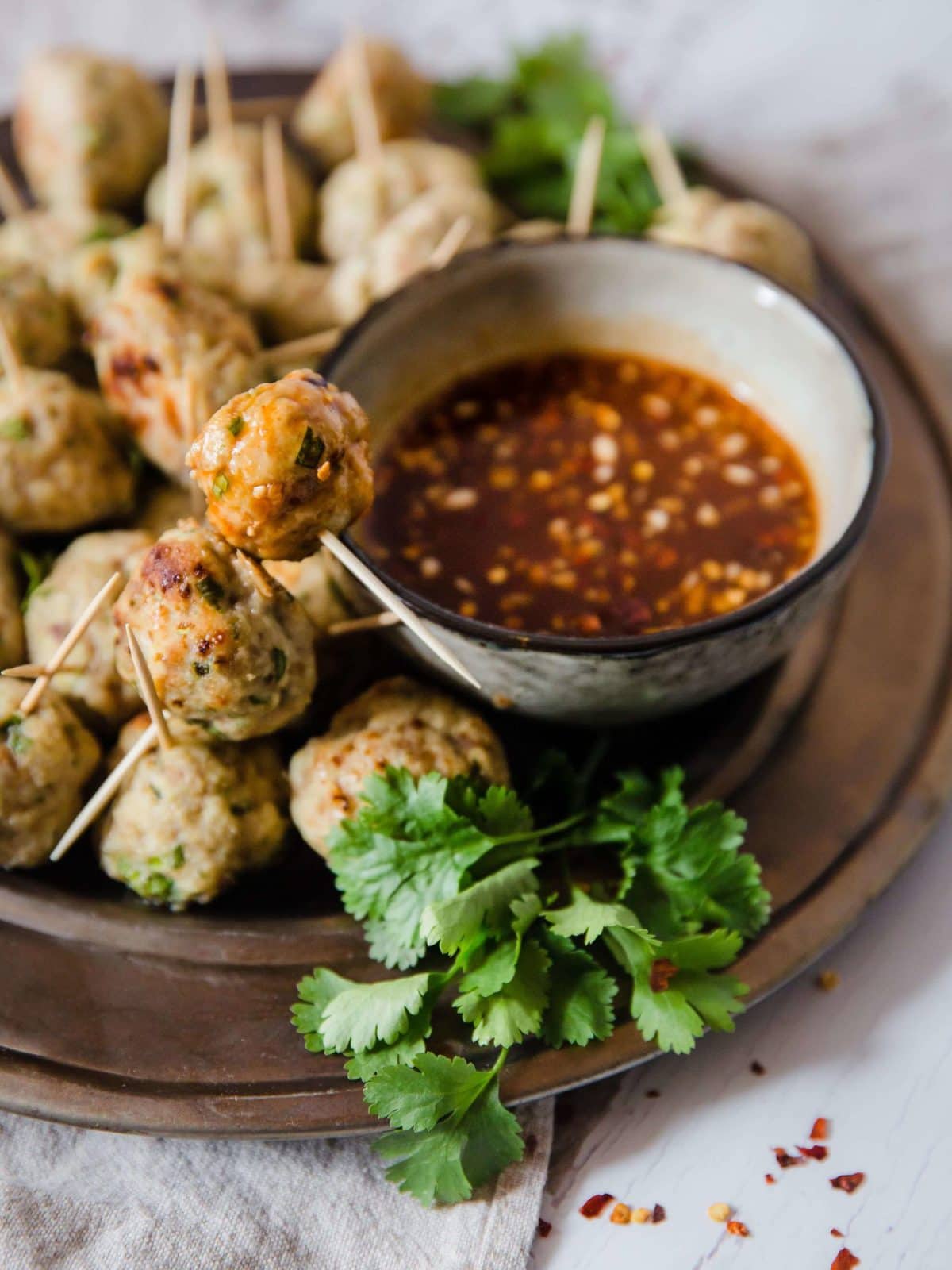 a platter of asian meatballs, served with dipping sauce and garnished with cilantro and red pepper flakes