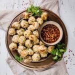 Asian Chicken Meatballs on a bronze plate with tooth picks, fresh herbs, and dipping sauce.