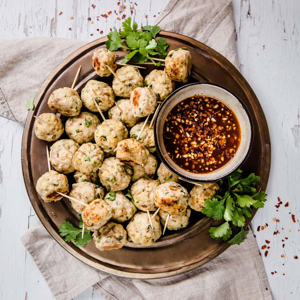 a serving tray full of chicken meatballs with toothpicks, served with sauce on the side and garnished with cilantro