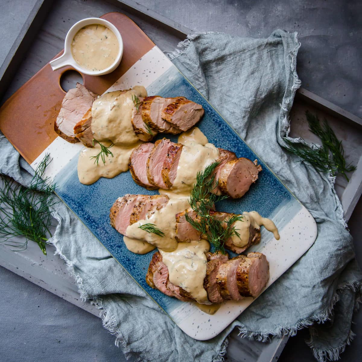 a blue serving tray with pork tenderloin medallions, topped with a creamy sauce and fresh dill
