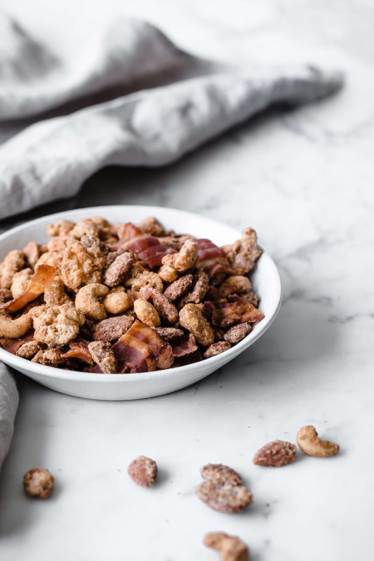 A ceramic bowl full of sugar free candied nuts with bacon and a gray towel in the background.