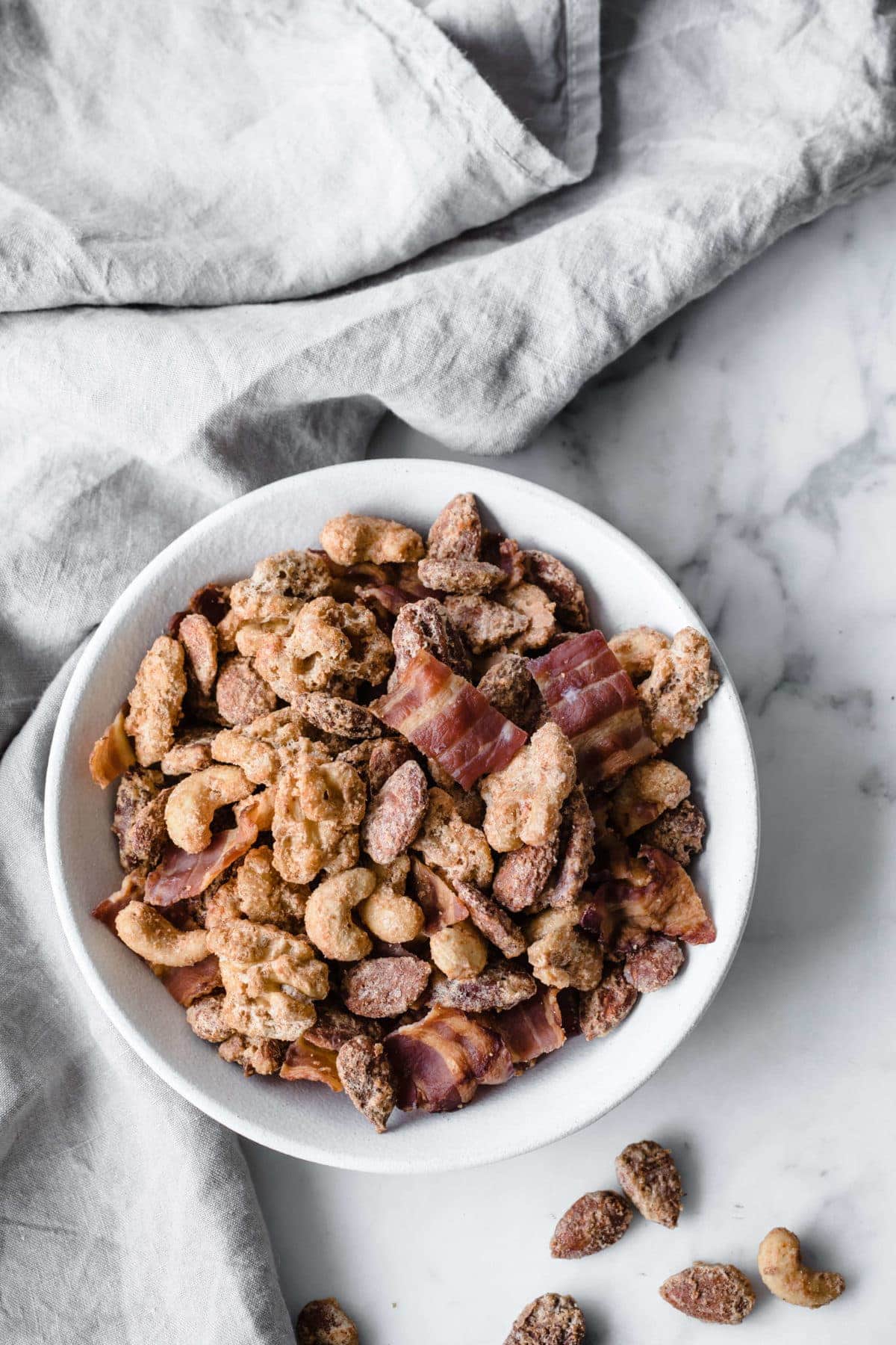 A ceramic bowl full of sugar free candied nuts with bacon and a gray towel in the background.