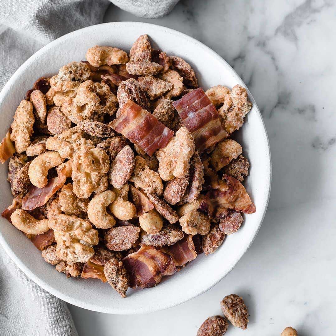 A ceramic bowl full of sugar free candied nuts with bacon and a gray towel in the background.