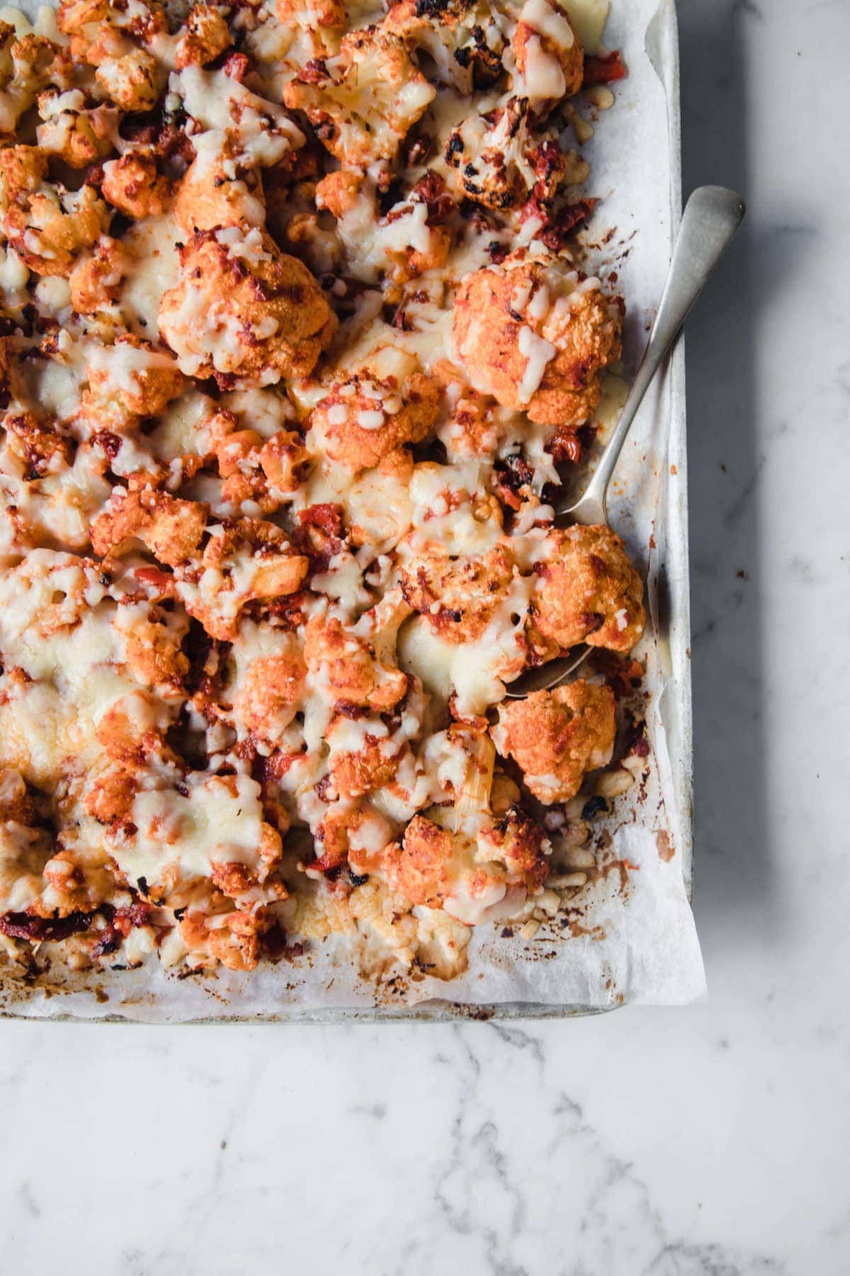 sheet pan lined with parchment paper and topped with roasted cauliflower, baked with cheese and pizza sauce