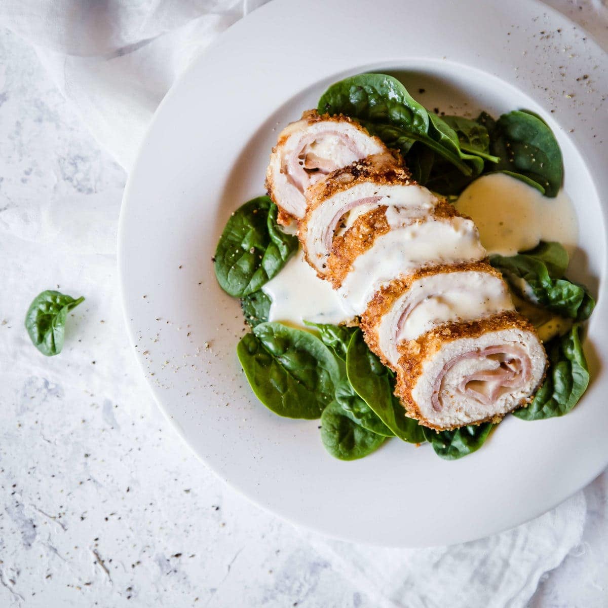 Overhead shot of sliced chicken Cordon Bleu, plated on baby spinach and topped with dijon cream sauce