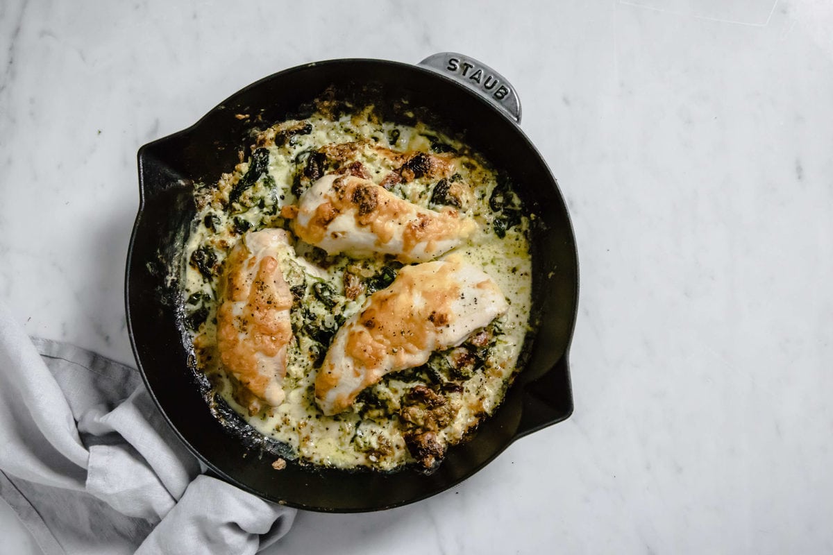 a cast iron skillet with a broccoli and cheese stuffed chicken  breast, covered with cheese and spices