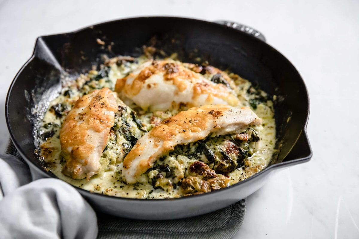 a cast iron skillet with a broccoli and cheese stuffed chicken  breast, covered with cheese and spices