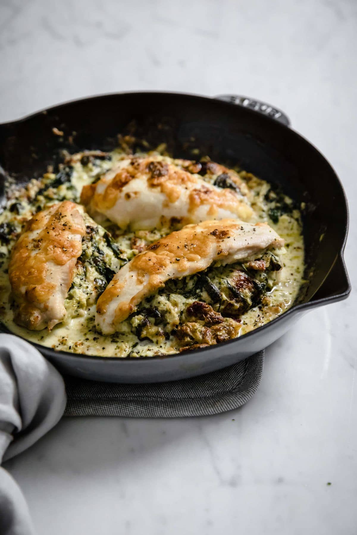 a cast iron skillet with a broccoli and cheese stuffed chicken  breast, covered with cheese and spices