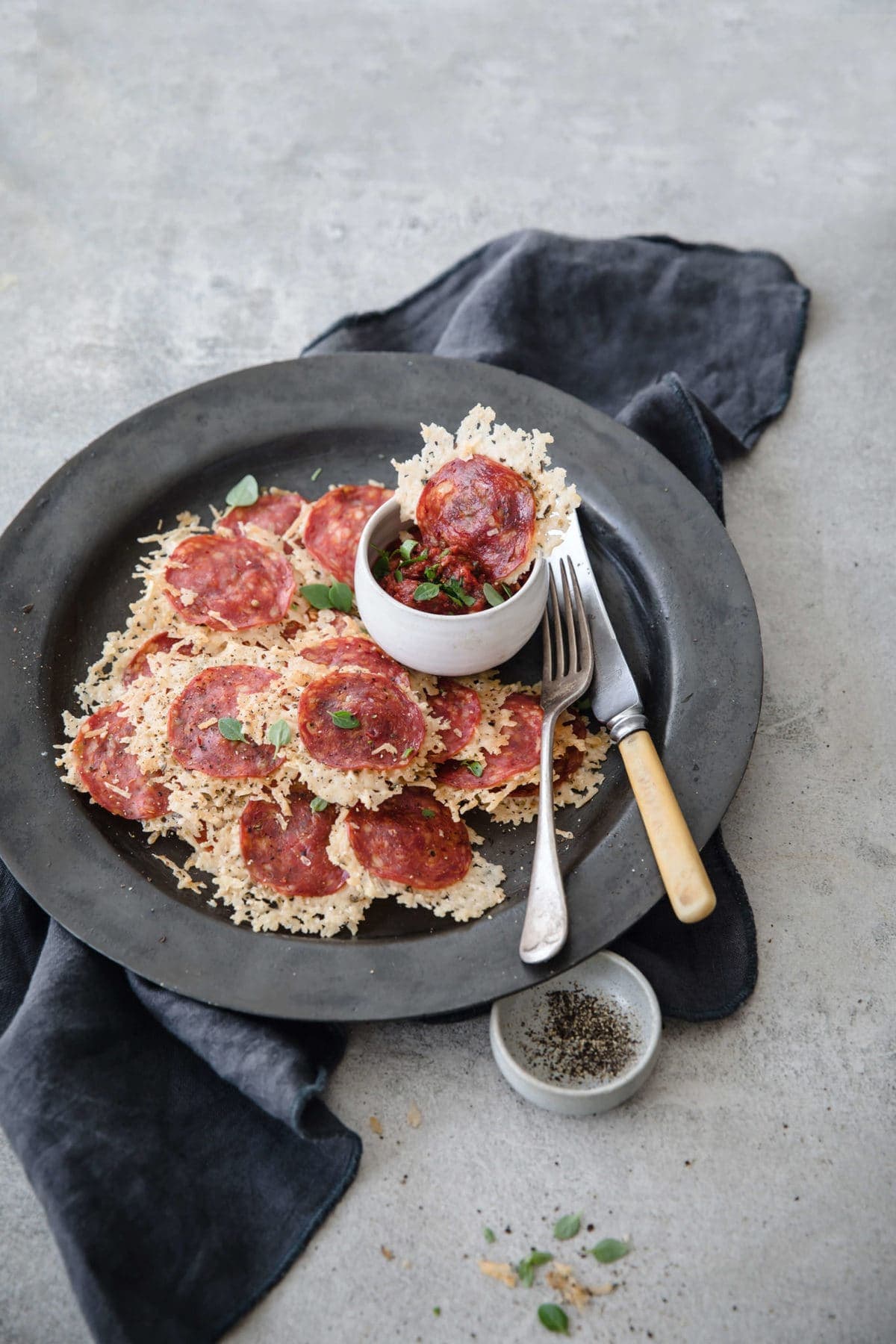 a gray plate loaded up with parmesan and pepperoni cheese pizza chips, with marinara and utensils on the side