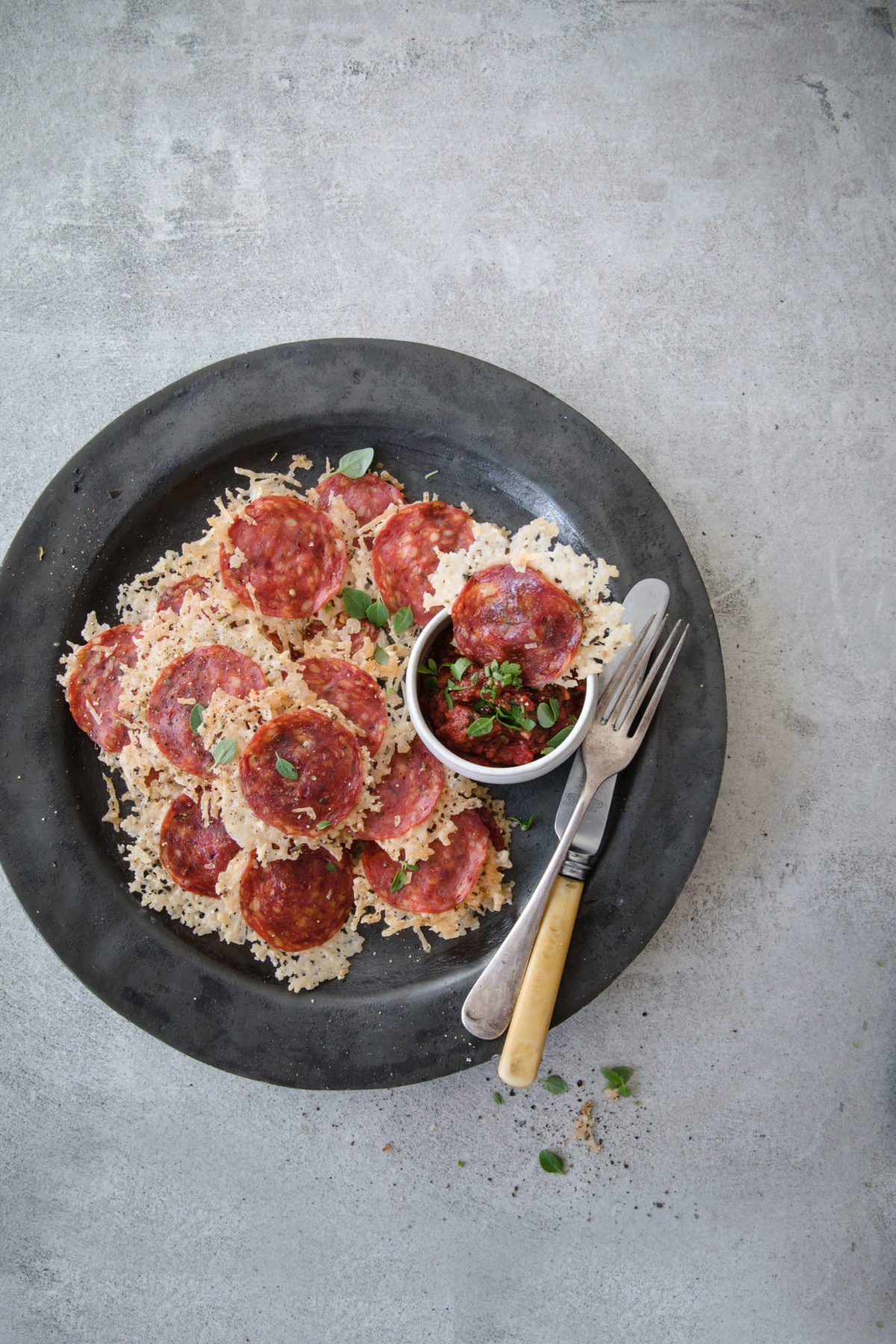 a gray plate loaded up with parmesan and pepperoni cheese pizza chips, with marinara and utensils on the side