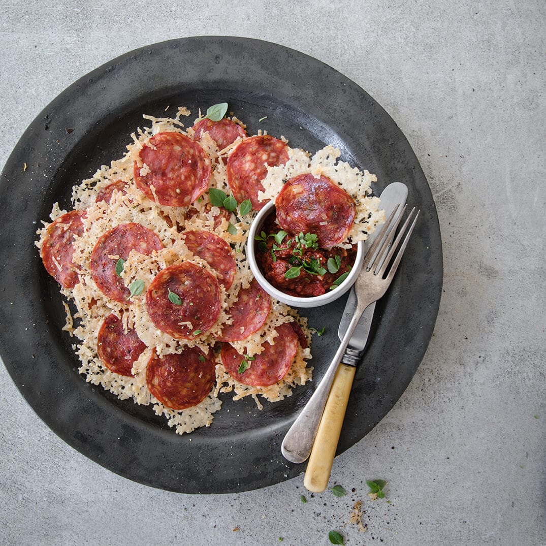 a gray plate loaded up with parmesan and pepperoni cheese pizza chips, with marinara and utensils on the side