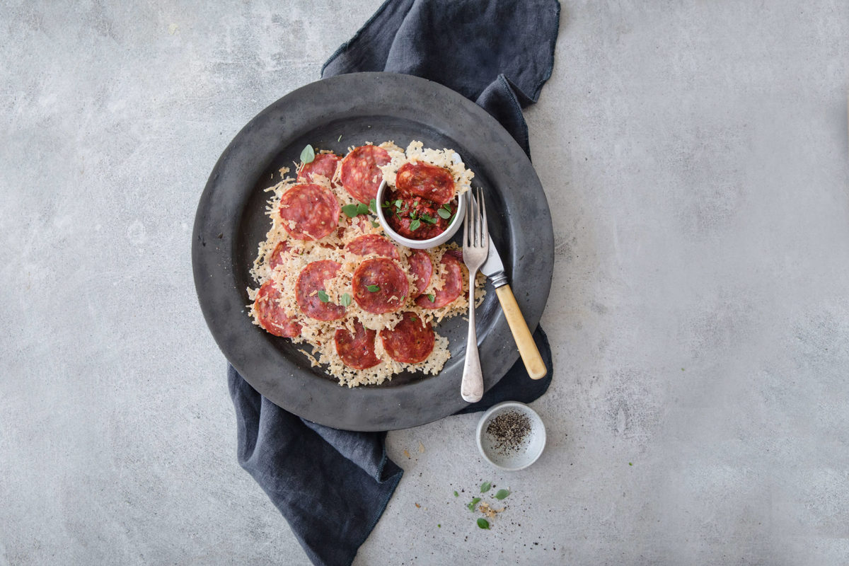 a gray plate loaded up with parmesan and pepperoni cheese crispy, with marinara and utensils on the side