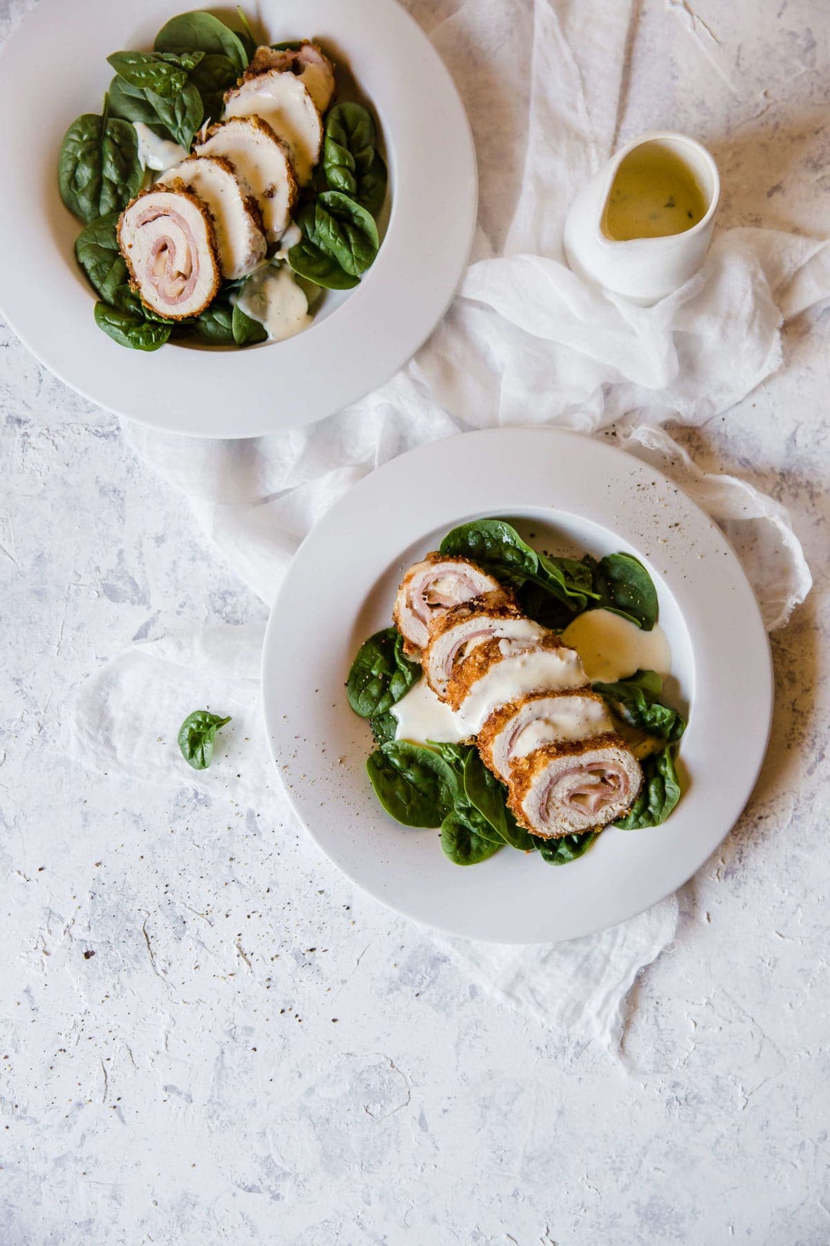 two white plates with fresh spinach leaves and sliced chicken Cordon Bleu, topped with cream sauce