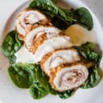 Sliced medallions of Keto Chicken Cordon Bleu on a bed of raw spinach in a white bowl, topped with creamy cheese sauce.