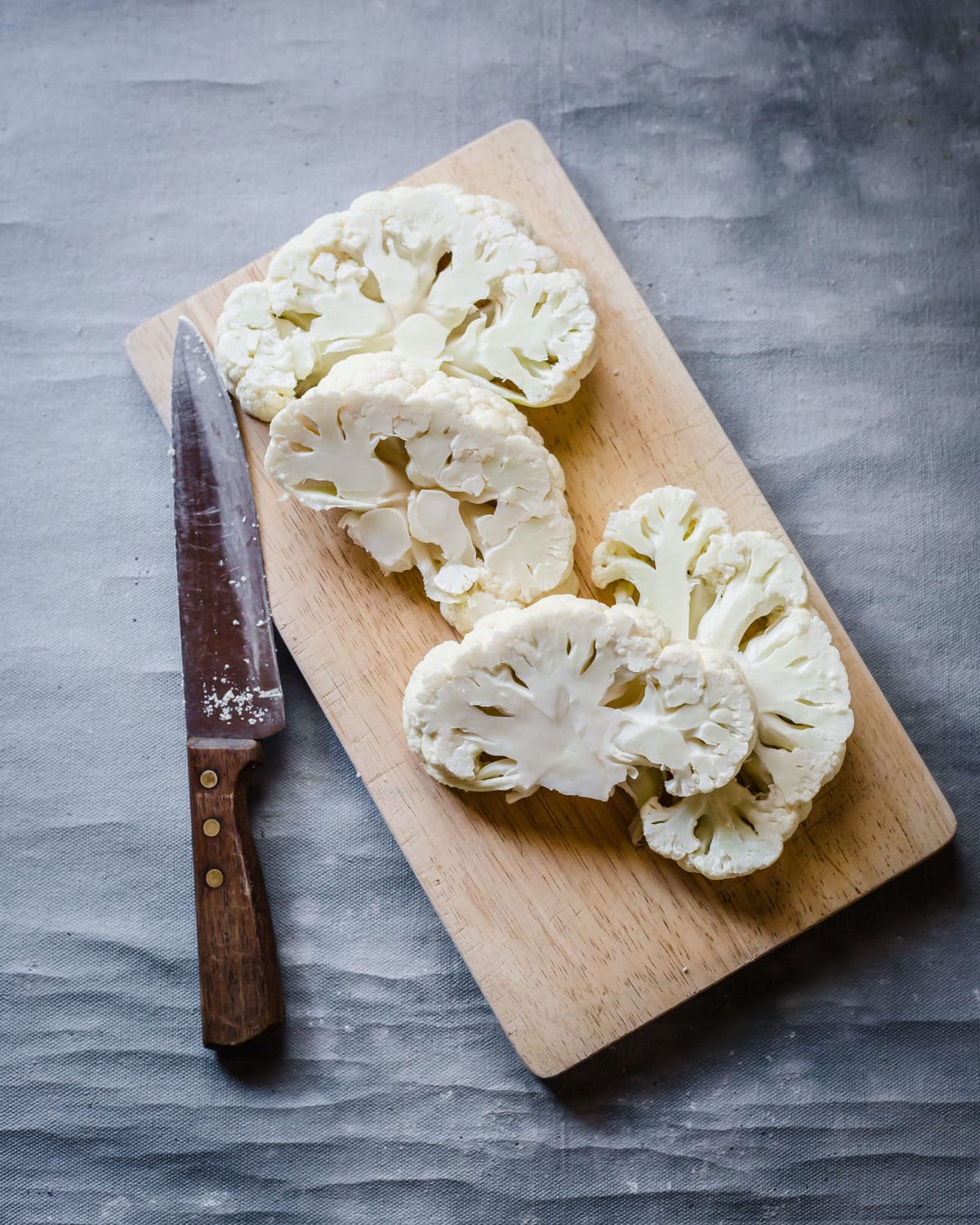 a wooden cutting board with 4 sliced cauliflower steaks and a knife. 