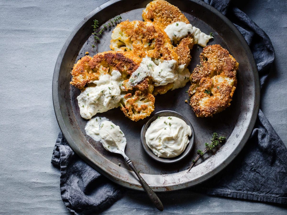 breaded and fried cauliflower steaks, served on a metal tray, with blue cheese dressing, garnished with parsley. 