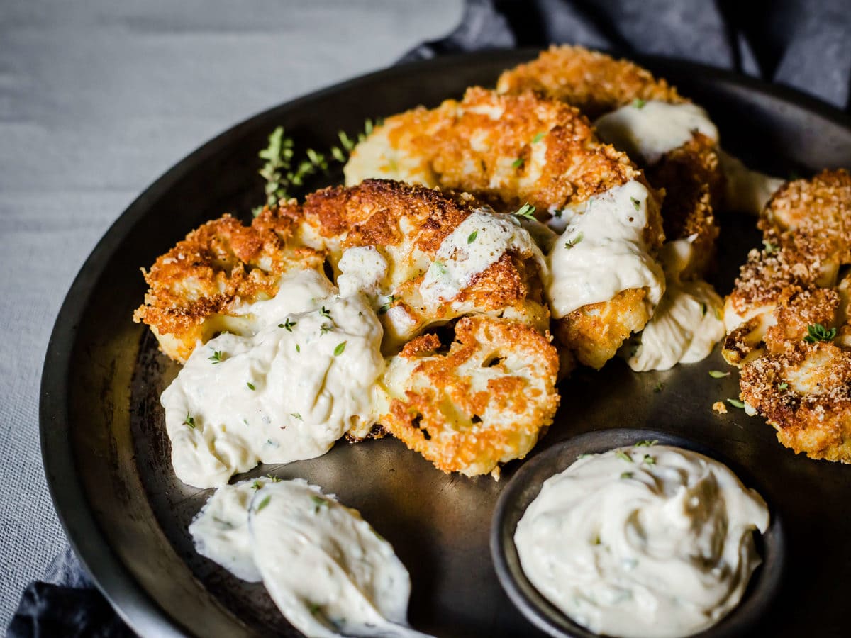 breaded and fried cauliflower steaks, served on a metal tray, with blue cheese dressing, garnished with parsley. 