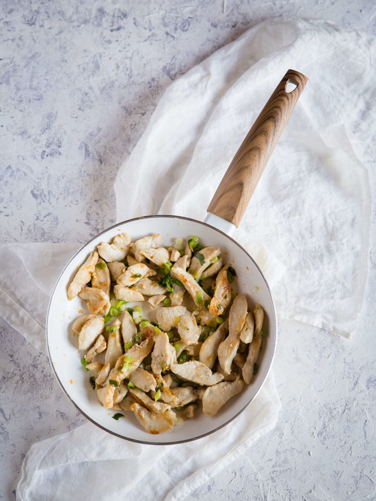 Sartén blanca con pollo salteado, cebollas verdes y salsa para una receta de Pad Thai sin gluten