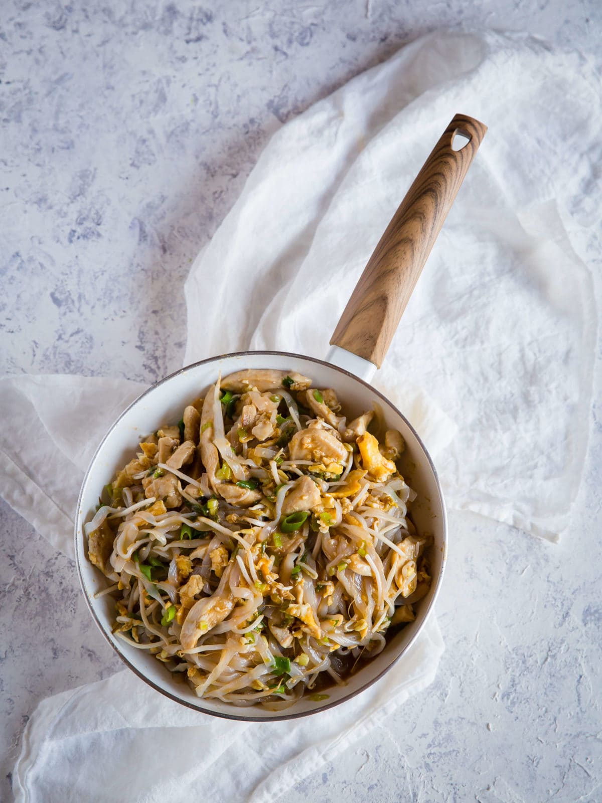 una padella con pollo saltato, cipolle verdi, aglio, uova, shirataki, cipolla verde, arachidi, per Pad Thai