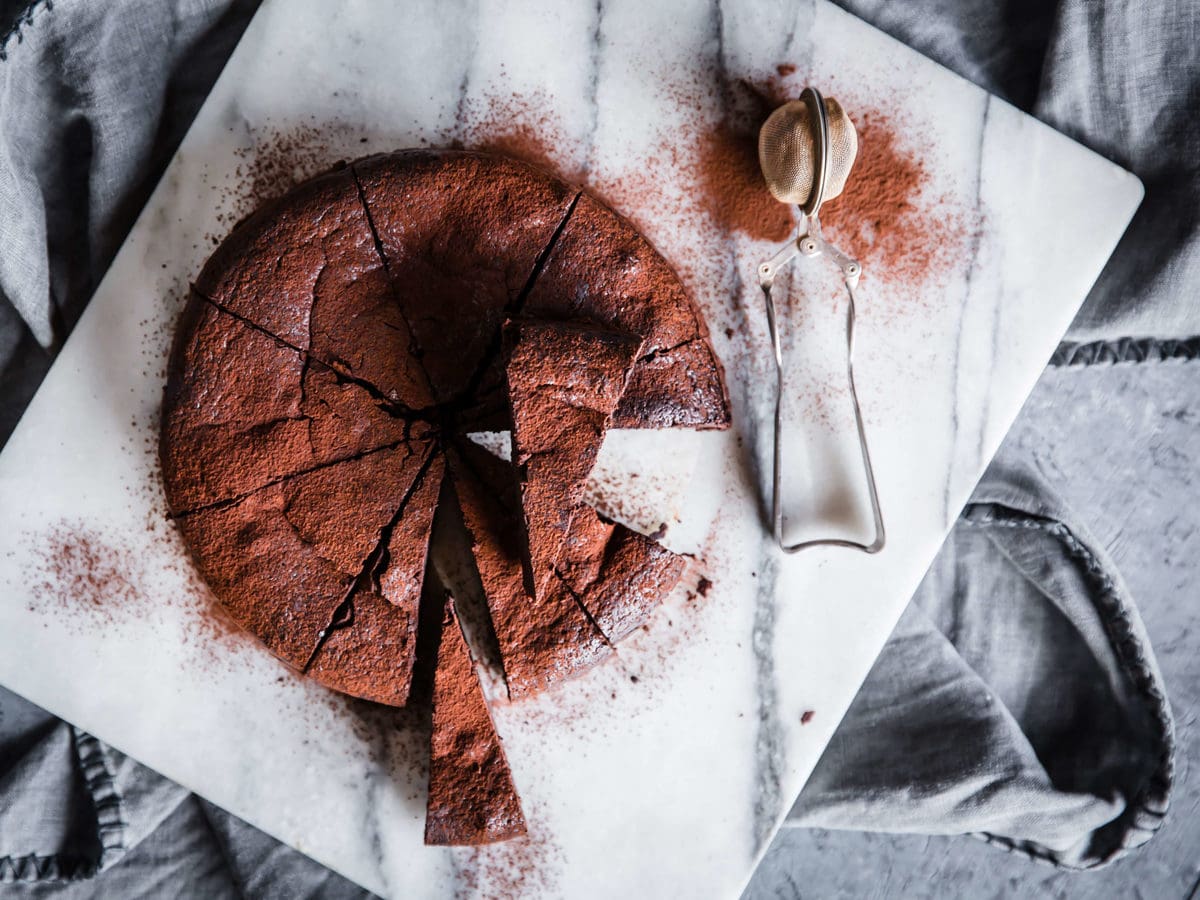 flourless chocolate cake on a slab of marble, sliced into 12 slices and dusted with cocoa powder