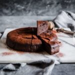 Keto Chocolate Espresso Flourless Cake cooling on a marble slab, cut into slices and dusted with cocoa powder using a baker's dusting wand.