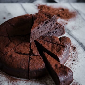 Keto Chocolate Espresso Flourless Cake cooling on a marble slab, cut into slices and dusted with cocoa powder.