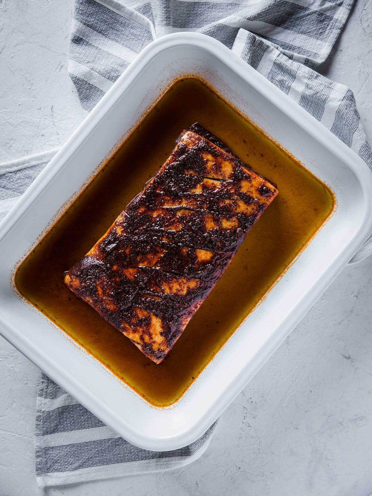 pork belly in a white baking dish, rubbed down with olive oil and coffee barbecue dry rub, surrounded by beef stock