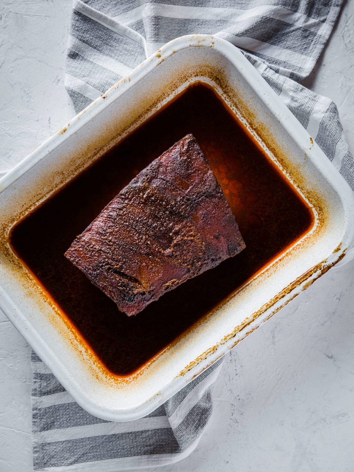 pork belly in a white baking dish, rubbed down with olive oil and coffee barbecue dry rub and baked in the oven