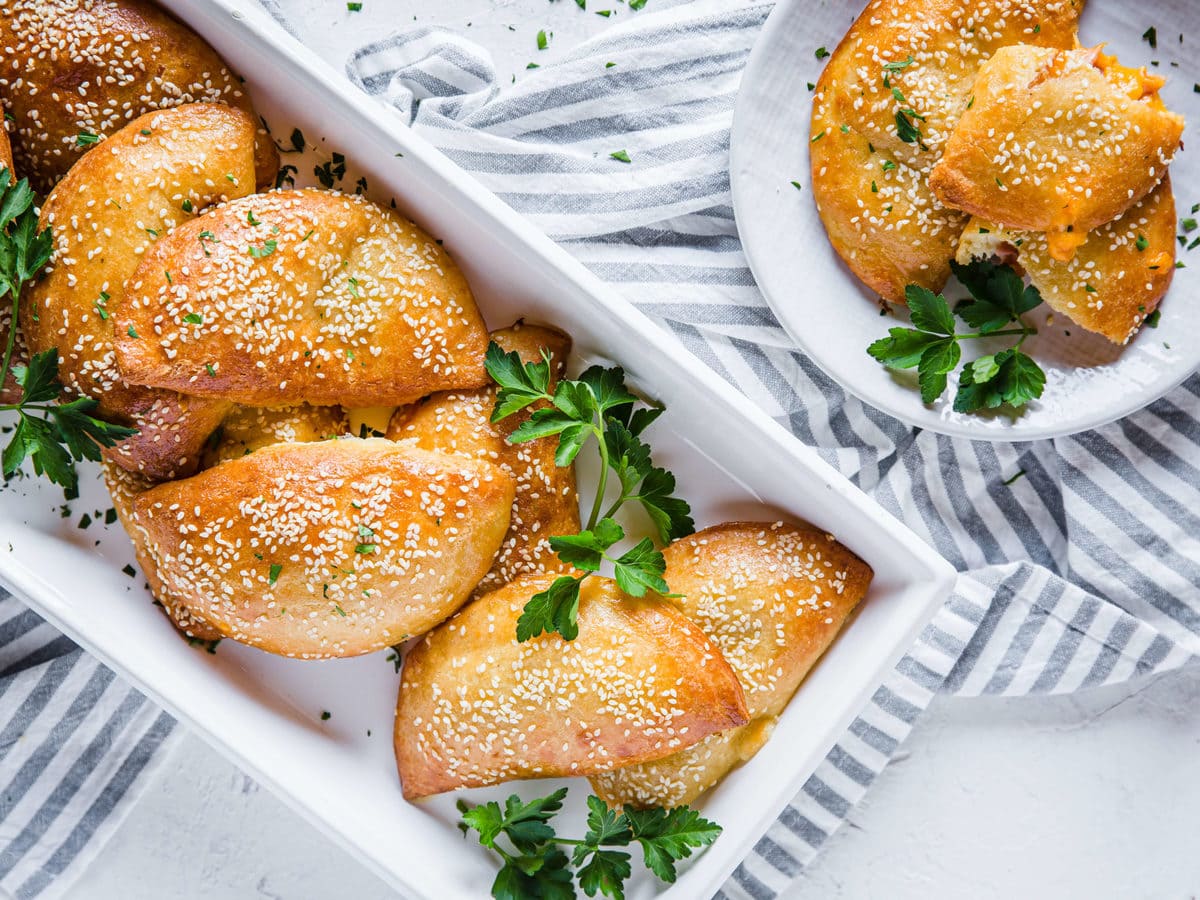 a serving tray filled with ham and cheese keto hot pockets topped with sesame seeds and garnished with fresh parsley 