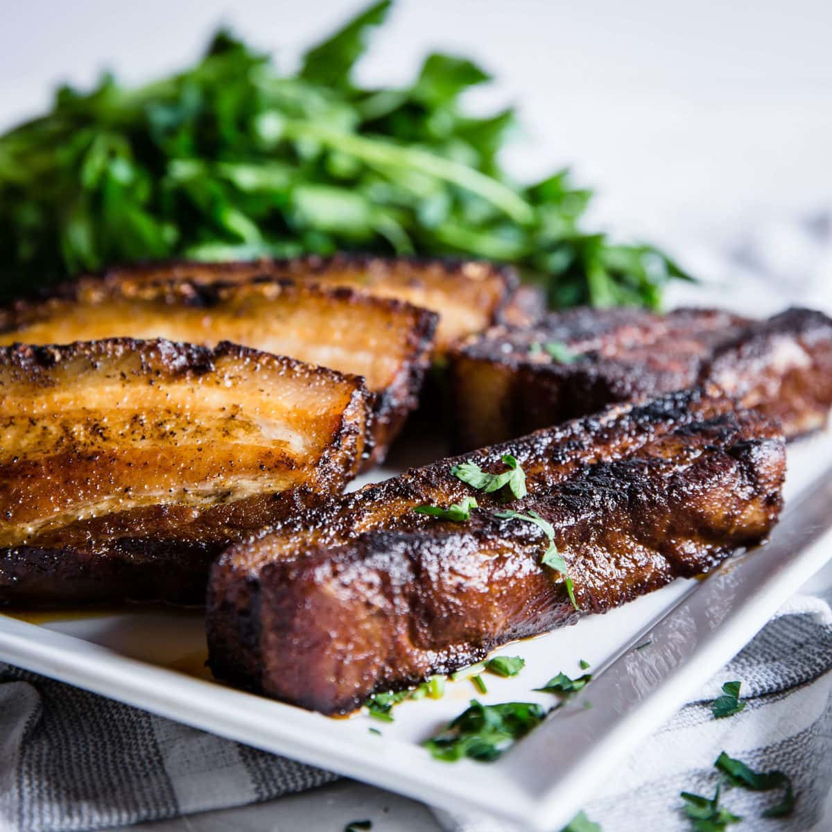 crispy sliced pork belly on a white plate, served with fresh greens