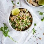 Keto Chicken Pad Thai garnished with red pepper flakes, cilantro, and lime in a white bowl on a white background with extra garnish sprinkled around.