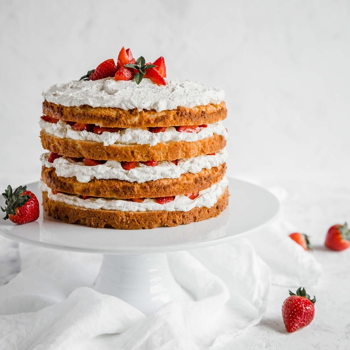 Keto Strawberry Shortcake with 4 layers of cake, whipped cream and strawberries on a cake stand.