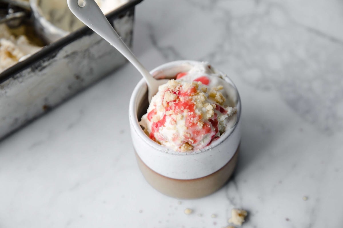 a small ceramic dish full of homemade strawberry cheesecake ice cream, with a white spoon.