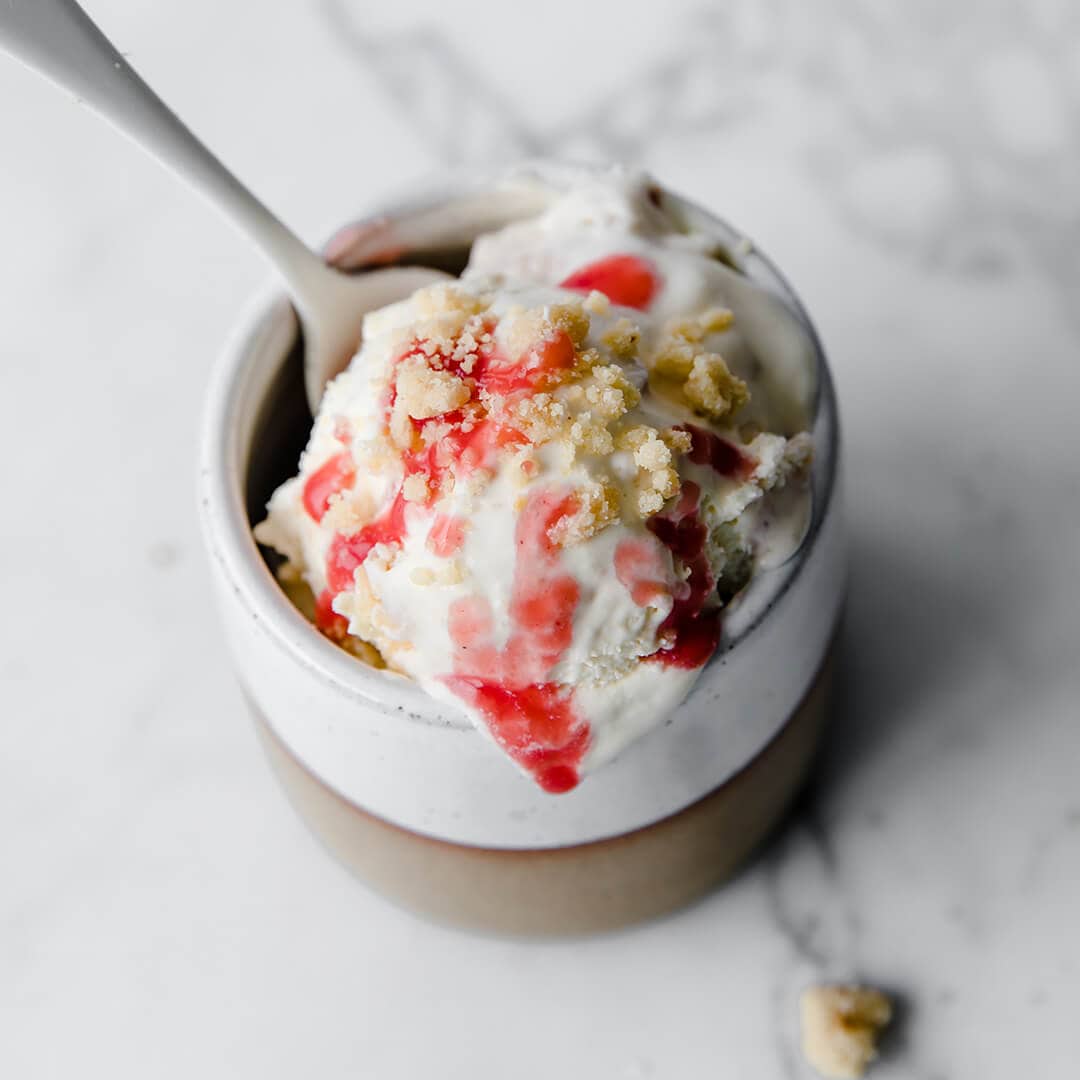 a ceramic serving dish with a homemade ice cream topped with strawberry sauce and a gluten free crumble