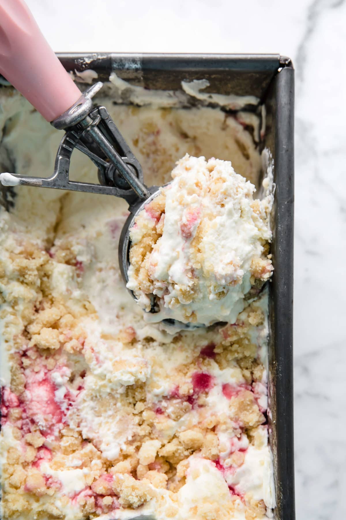 a vintage loaf pan full of homemade ice cream with strawberry sauce and a gluten free crumble on top.