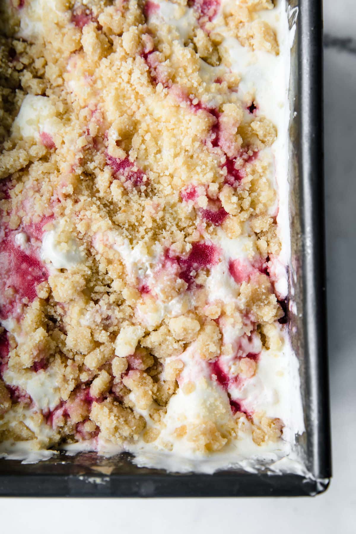 a vintage loaf pan full of homemade ice cream with strawberry sauce and a gluten free crumble on top.