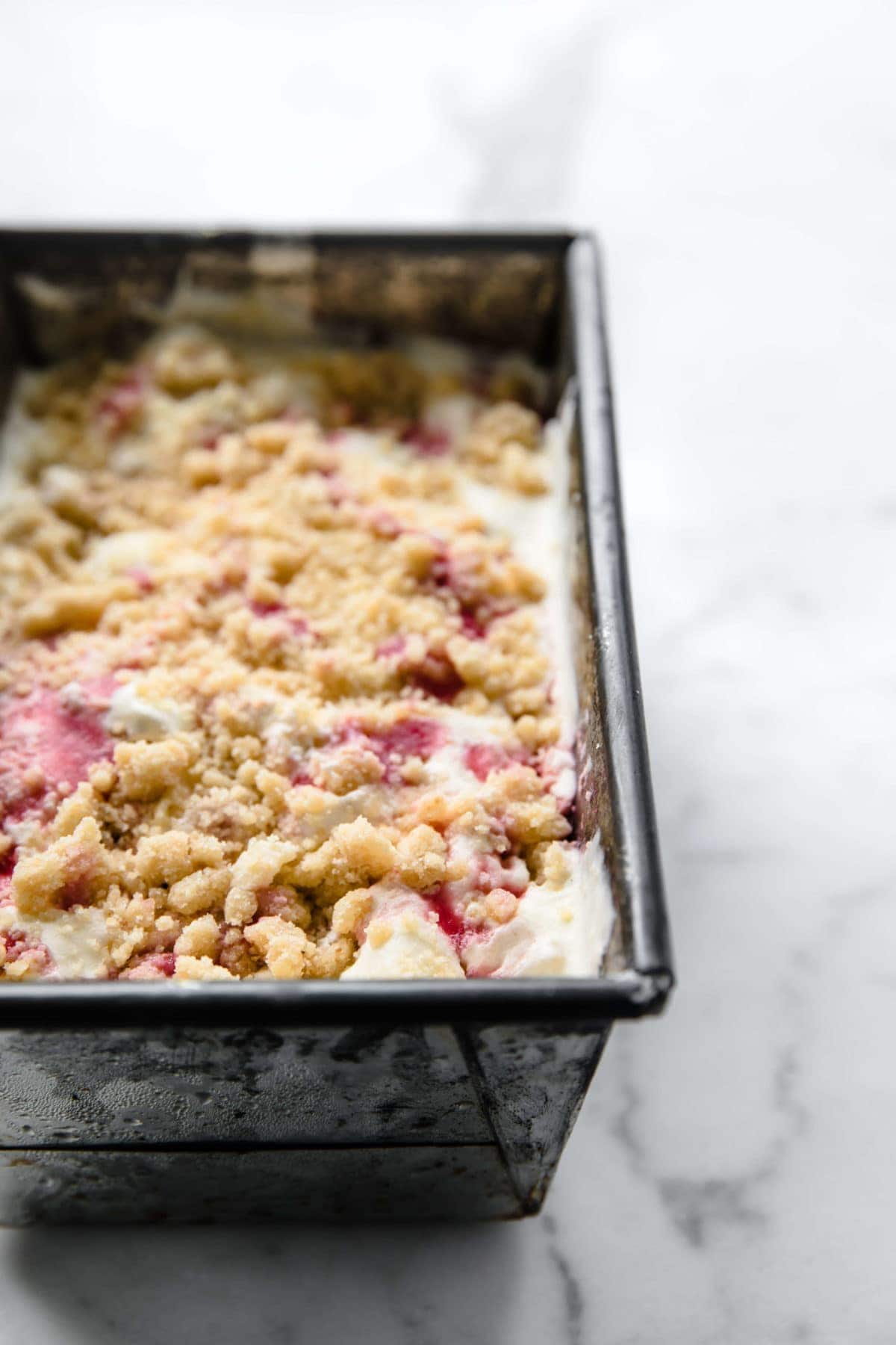 a vintage loaf pan full of homemade ice cream with strawberry sauce and a gluten free crumble on top.