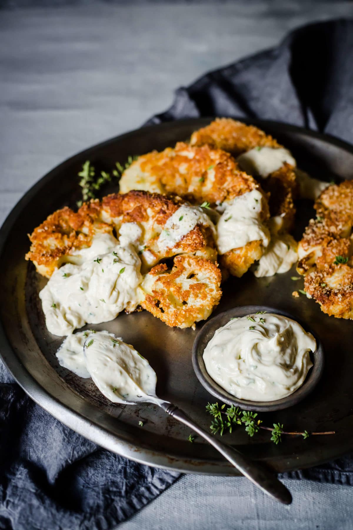 breaded and fried cauliflower steaks, served on a metal tray, with blue cheese dressing, garnished with parsley. 
