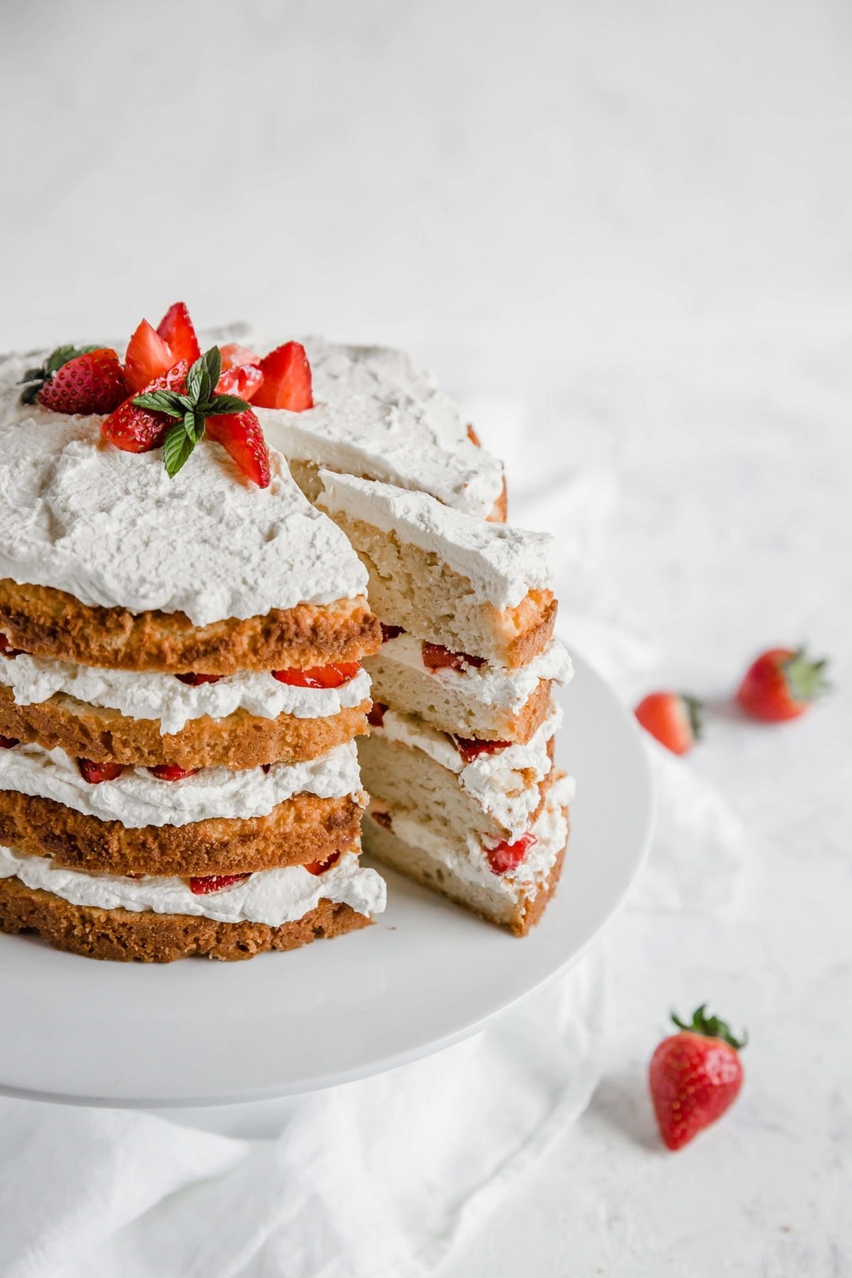 Strawberry shortcake with a slice cut out of it - cake, layered with whipped cream and strawberries