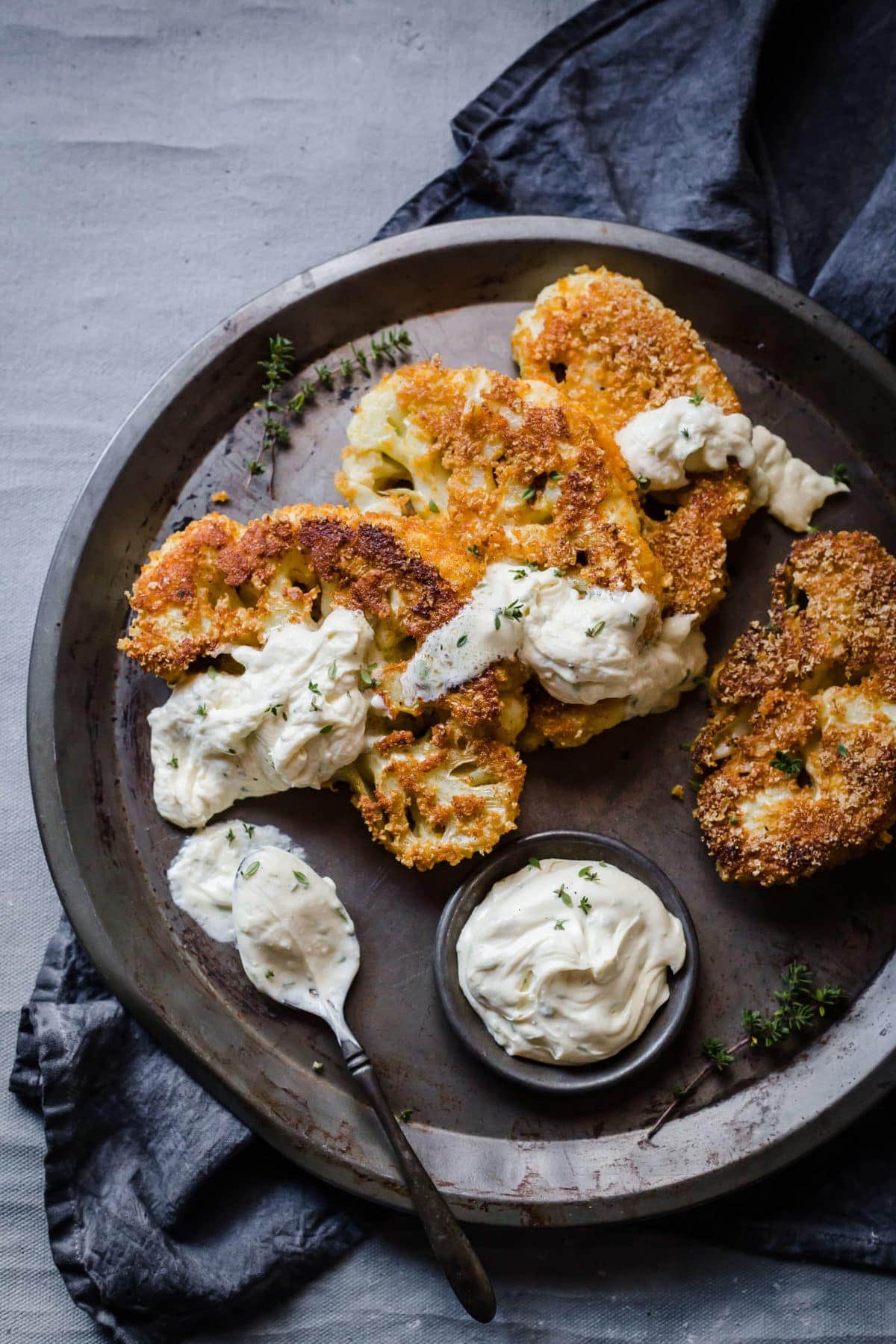 breaded and fried cauliflower steaks, served on a metal tray, with blue cheese dressing, garnished with parsley. 