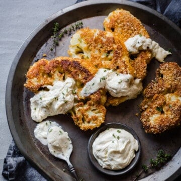 breaded and fried cauliflower steaks, served on a metal tray, with blue cheese dressing, garnished with parsley.