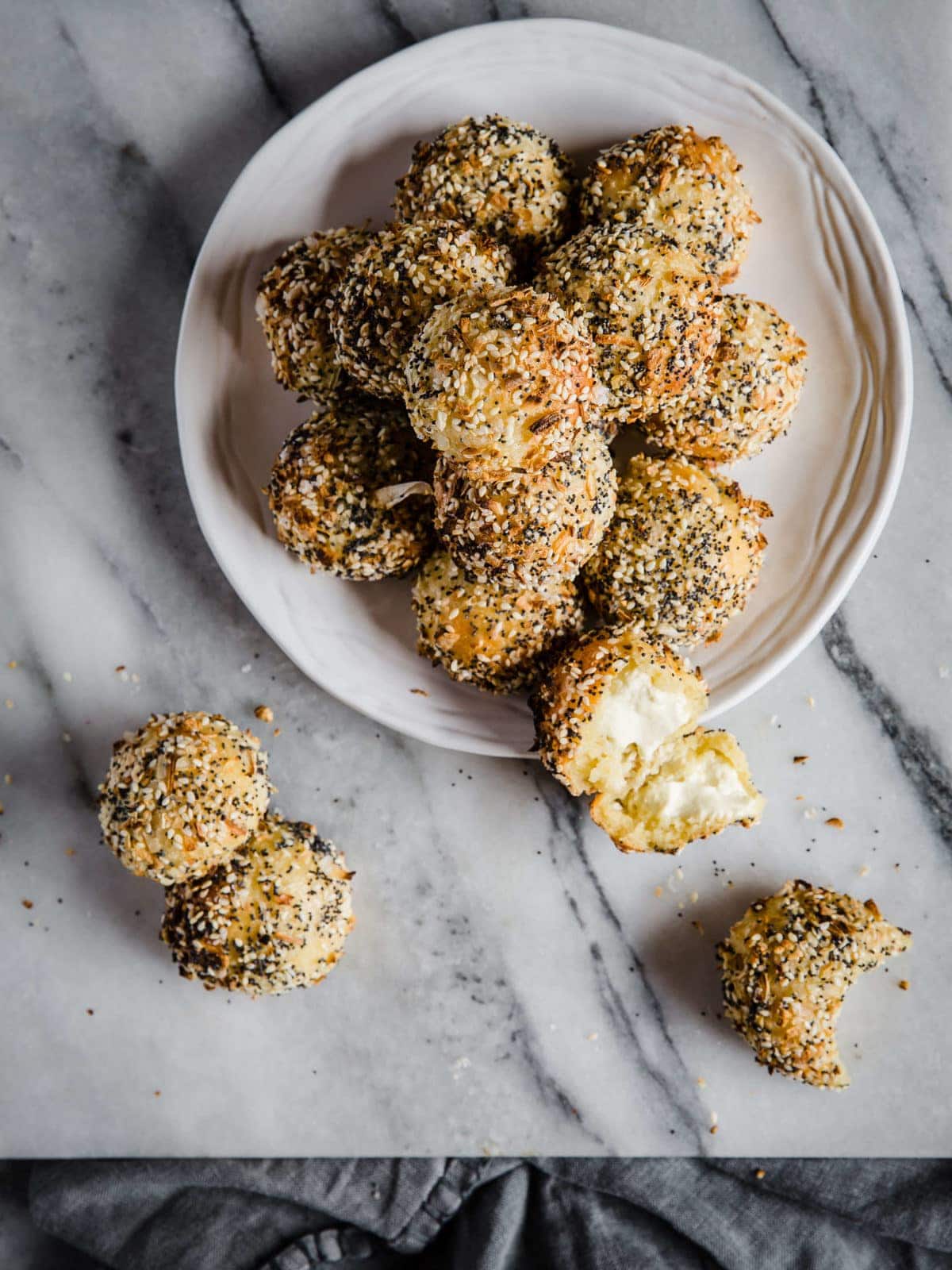 A white plate piled high with low carb cream cheese stuffed bagel bites - coated generously with everything bagel seasoning.