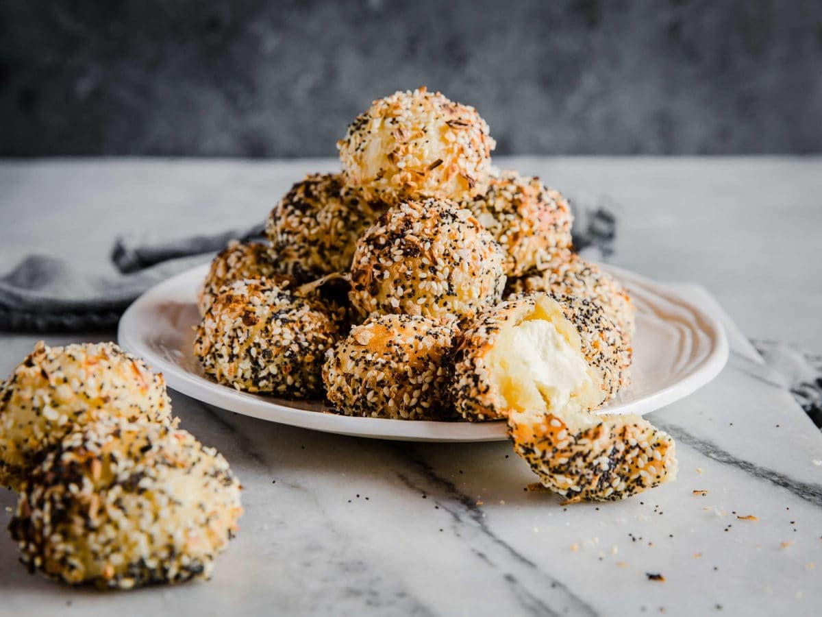 A white plate piled high with low carb cream cheese stuffed bagel bites - coated generously with everything bagel seasoning.