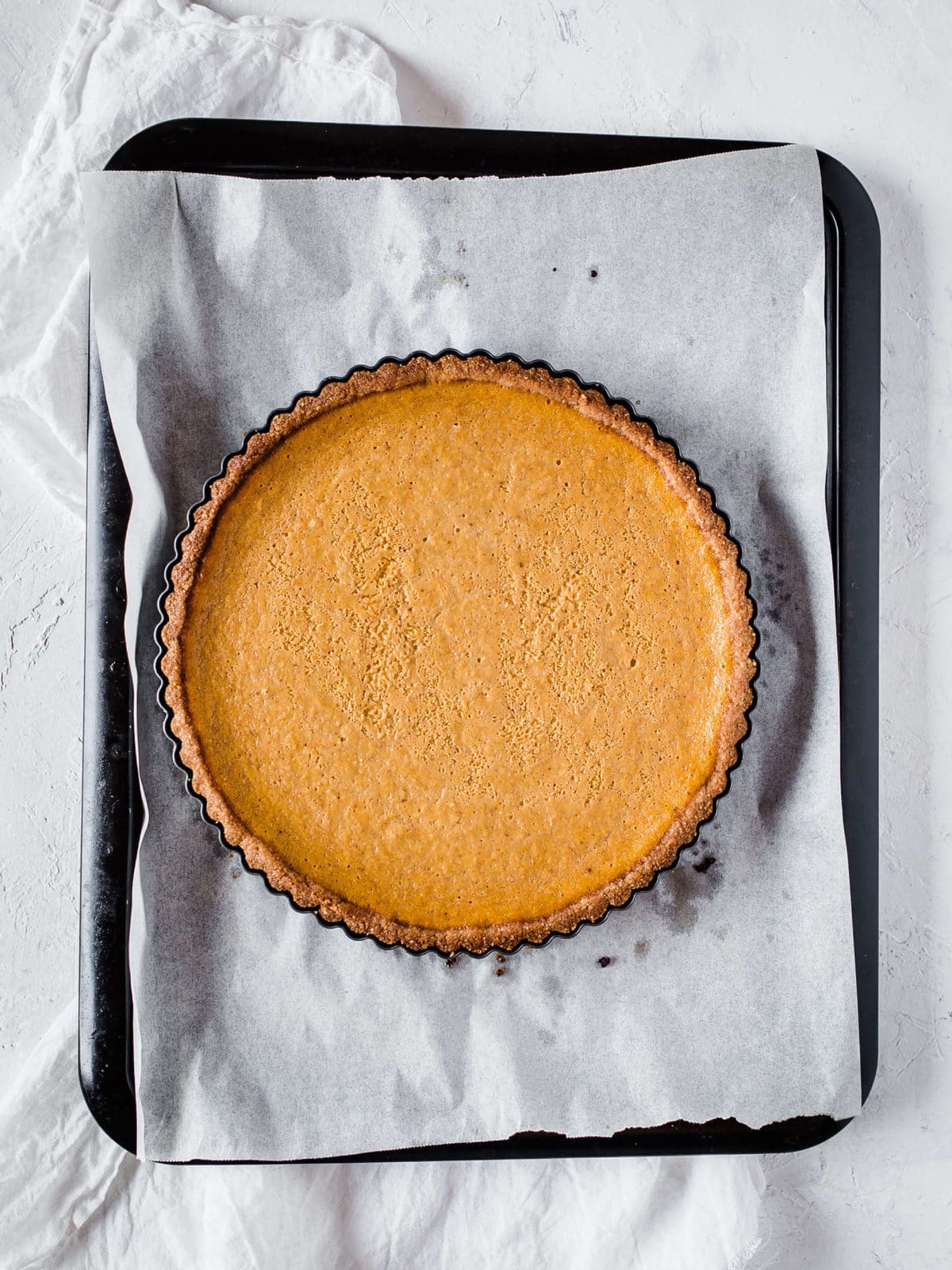 a fresh baked pumpkin pie, right out of the oven, on a parchment lined baking sheet.